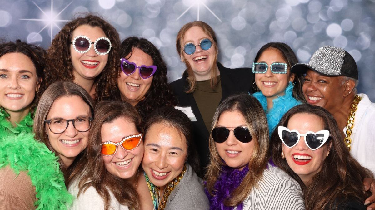 Group of 8 women smiling wearing glasses in photobooth